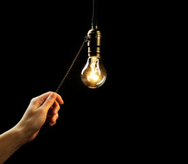 Female hand turning on light bulb on black background, close up - obrazy, fototapety, plakaty