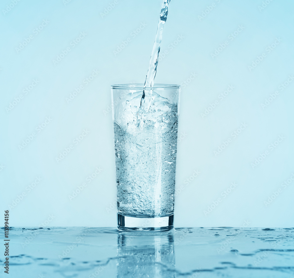 Wall mural Pouring water into glass on light background