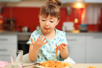 Adorable little girl eating spaghetti at table