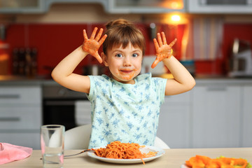 Adorable little girl eating spaghetti at table