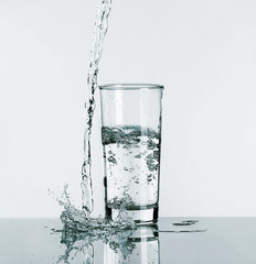 Pouring water into glass on light background