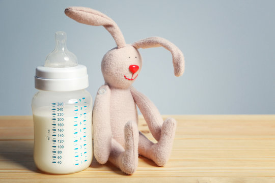 Baby bottle with milk with rabbit toy on wooden table