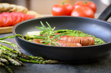sausages with asparagus, tomatoes and rosemary on a pan