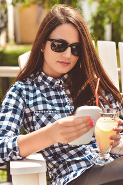 Young woman with phone and sunglasses drinking lemonade in an cafe. Toned Image