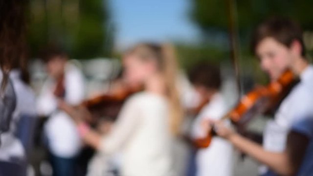 Out focus of Kids play violin at outdoor performance group.