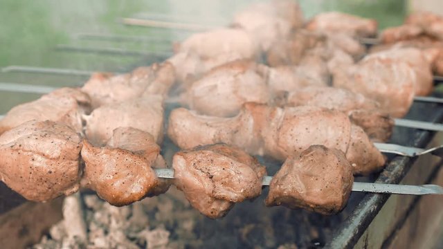 Barbecue skewers with meat cooking on the grill outdoors with smoke. Closeup detailed shot. 4K UHD video footage.