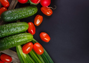 Background of blank black color with fresh healthy vegetables, green onion, radish, cucumber, tomatoes. Empty space for text. Top view.