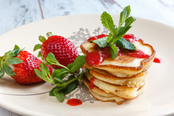 Freshly pancakes with garden fresh strawberries and mint on a bright plate, photographed in daylight natural light.