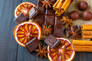 Dark and milk chocolates with dry oranges, candies, cinnamon and anise on burlap on rustic wooden...