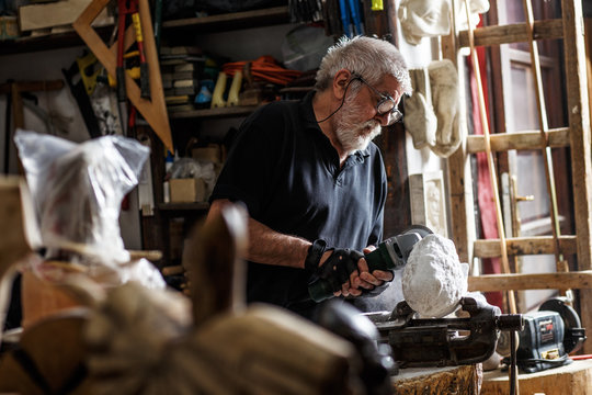 Senior Sculptor Working On His Marble Sculpture In His Workshop With Grinder.