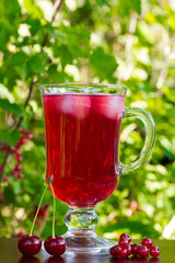 a glass of red cherry juice with ice cubes and cherries and red currants on a natural background. selective focus