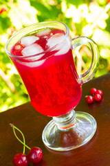 a glass of red cherry juice with ice cubes and cherries and red currants on a natural background. selective focus, unusual angle