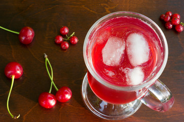 a glass of red cherry juice with ice cubes and cherries and red currants on a wooden background closeup. selective focus, top view