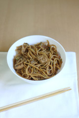 Noodles with chicken and various vegetables. Served in a white bowl with chopsticks. Selective focus. 