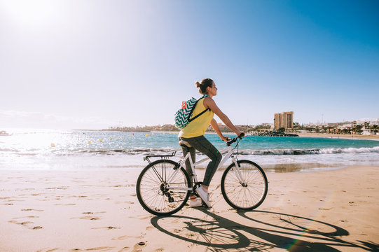 carefree woman with bicycle riding on beach sand having fun and