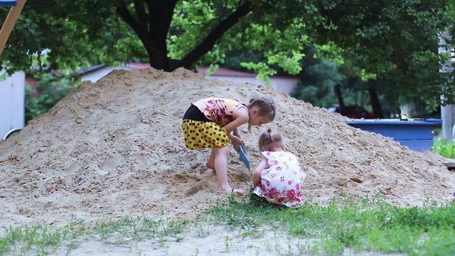 Two little girls sister playing in the sandbox shoulder blades in the park