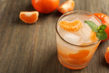 One fresh delicious tangerine cocktail with ice, mint and mandarins on the wooden table, close up