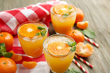 Tangerine cocktails with sliced mandarins, ice, mint with striped straws on a wooden table, close up