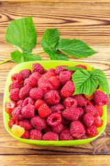 Bowl full of ripe raspberries on rustic wooden table.