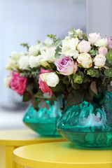 Beautiful bouquet of colourful roses in glass vase on yellow table