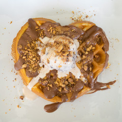 Waffle with a shape of a heart having a ball of stracciatella ice cream on top of it.

