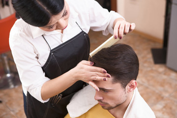 Handsome man having his hair cut by barber girl. View of hairdresser combing handsome man's in hairdressing saloon.