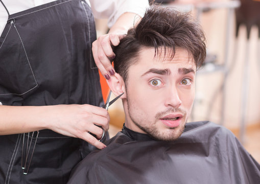 Closeup picture of handsome man having his hair cur by professional hairdresser in hairdressing saloon. Young man looking at camera.