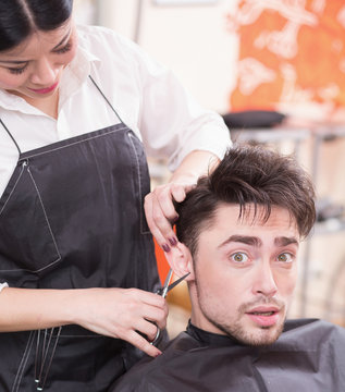 Picture of handsome man having his hair cur by professional hairdresser in hairdressing saloon. Young man looking at camera.