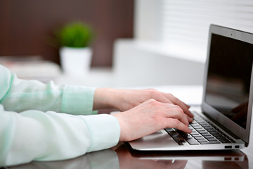 Business woman hands in a green blouse sitting at the desk in the office and typing on the laptop .