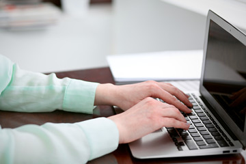 Business woman hands in a green blouse sitting at the desk in the office and typing on the laptop .