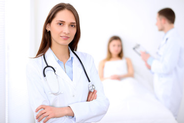 Fototapeta premium Friendly female doctor on the background with patient in the bed and his doctor