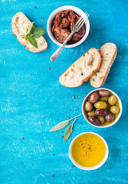 Mediterranean Snacks Set. Olives, Oil, Sun-dried Tomatoes, Herbs And Sliced Ciabatta Bread On Over Blue Painted Background