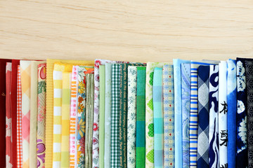 Stack of multi-colored fabrics with different textures on wooden background.