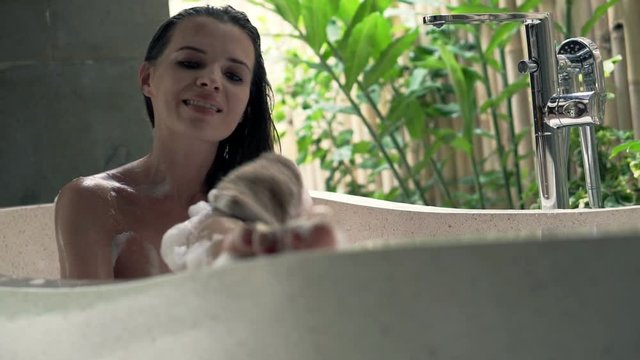 Young woman in bathtub washing her legs in open bathroom 
