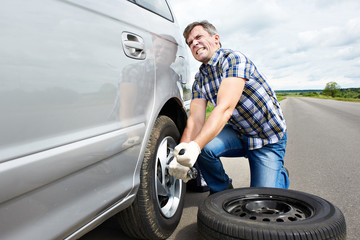 Man changing a spare tire of car