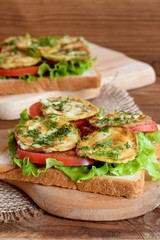 Sandwiches with fresh lettuce, sliced tomato, grilled zucchini dill and garlic. Sandwiches on a kitchen cutting board, burlap and wood background. Lunch food to work, school, picnic