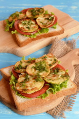 Sandwiches with lettuce, tomato, zucchini, dill and garlic. Vegetable sandwiches on a cutting board and blue background. Vegetarian healthy lunch recipe. Vegetable diet food
