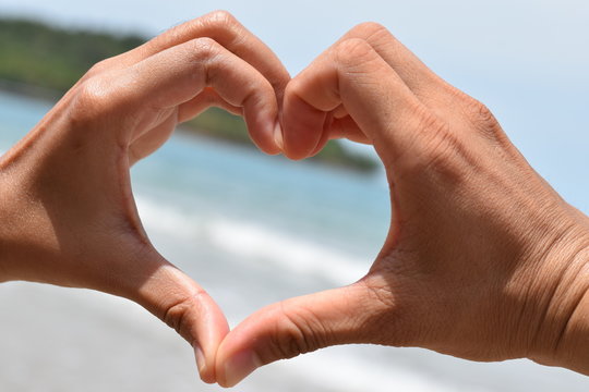 Hands in the shape of a heart on a background of blue sea