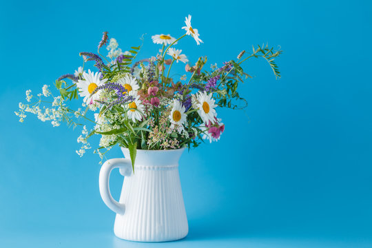 bouquet of wildflowers in jar on plain blue background