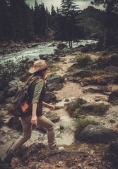 Naklejka premium Woman hiker jumping on the stones near wild mountain river.