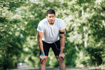 Tired sportsman standing and resting after jogging in park