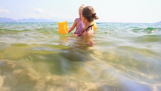 Blond Mother Holds in Arms Little Daughter in Azure Sea