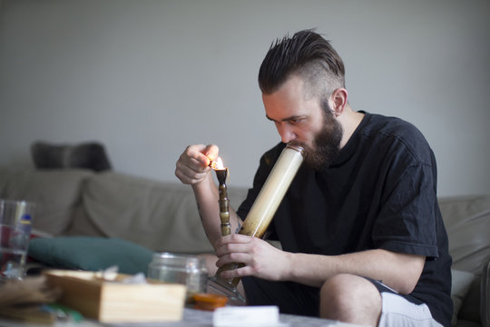 Young Man Smoking Drugs In Bong At Home