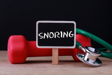 Medical concept - Stethoscope and dumbbell on wood with Snoring word