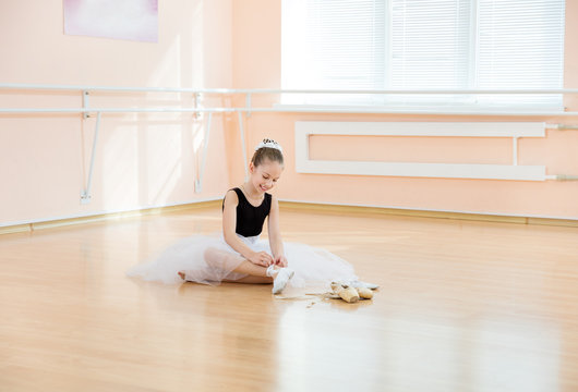 Young balerina changing dancing shoes to pointe ones while sitting on floor 