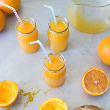 Freshly squeezed orange juice in jar with drinking straw on metallic countertop. Selective focus.