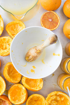 White bowl with wooden squeezer, squeezed oranges and fresh orange juice in jars. Selective focus on squeezer.