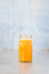 Freshly squeezed orange juice in jar with drinking straw on metallic countertop. Selective focus.
