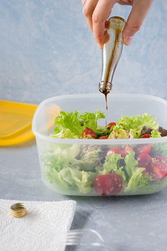 Pouring italian dressing from small bottle into takeaway container with fresh lettuce and cherry tomatoes salad. Selective focus.