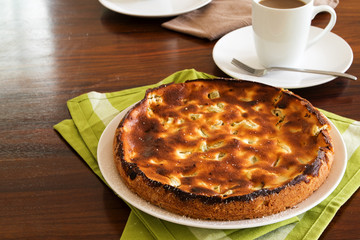 cheesecake with rhubarb on a kitchen towel and coffee cup on a brown wooden table